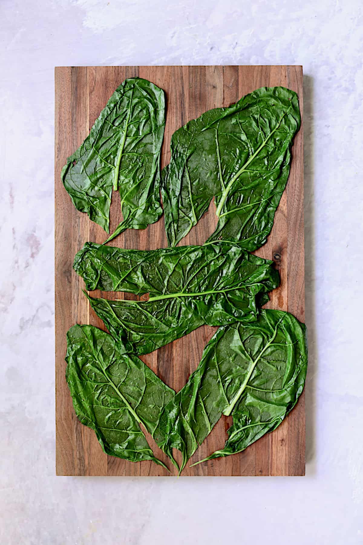 Photo of blanched Swiss chard leaves on wood cutting board.
