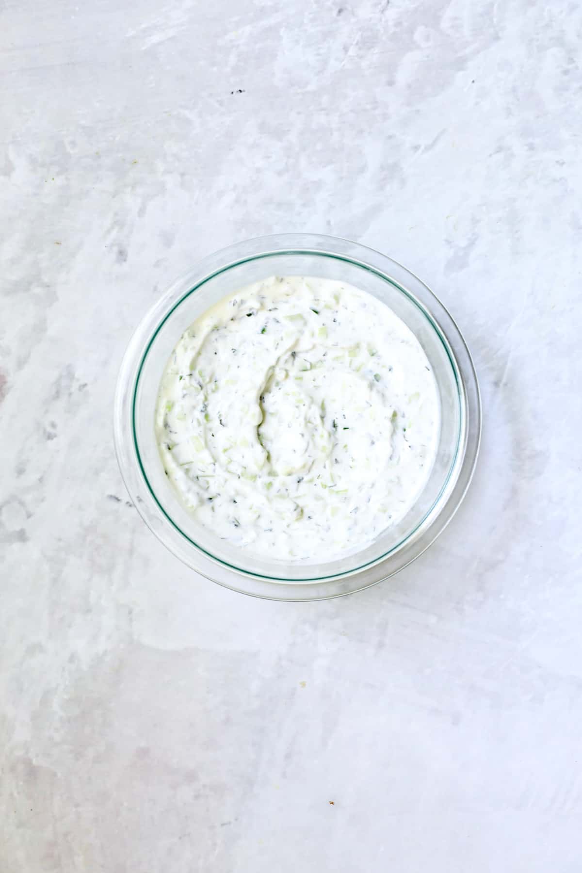 Photo of tzatziki sauce in glass bowl on marble background.