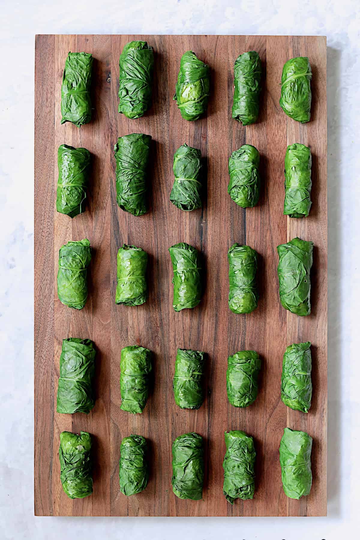Photo of 25 Quinoa-Stuffed Swiss Chard Dolmas on wood cutting board.
