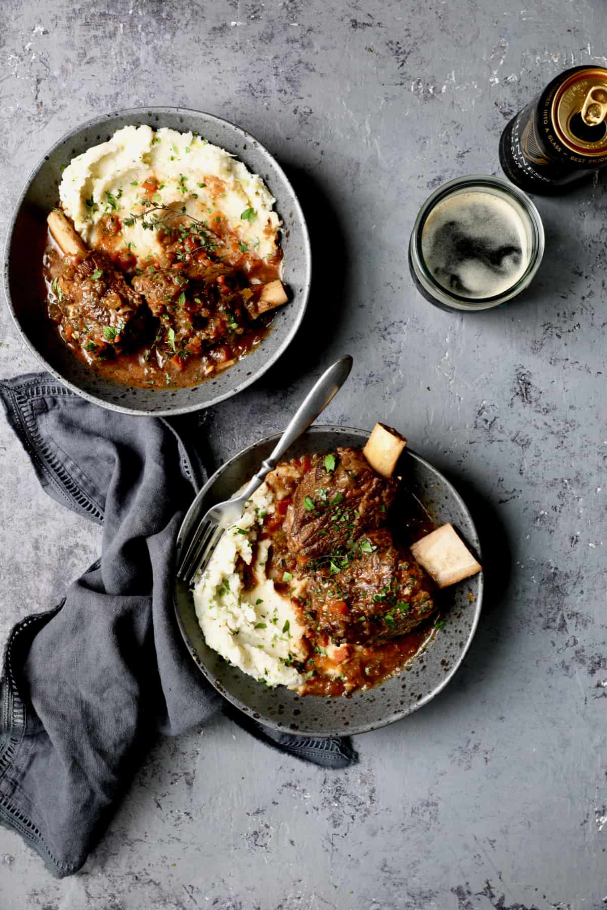 Photo of Stout Braised Beef Short Ribs and Colcannon with glass of beer on gray background.
