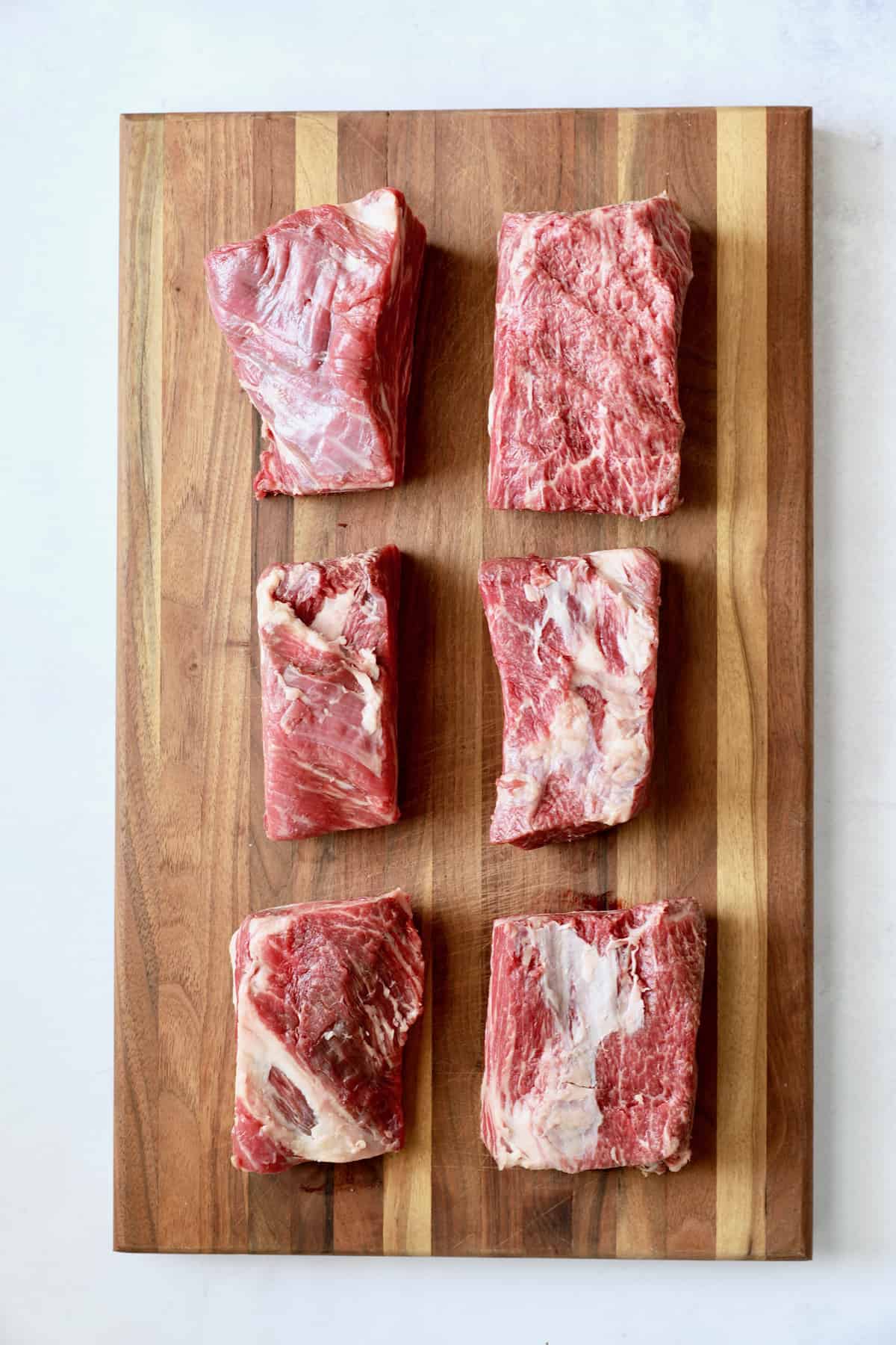 Photo of six uncooked beef short ribs on wood cutting board.