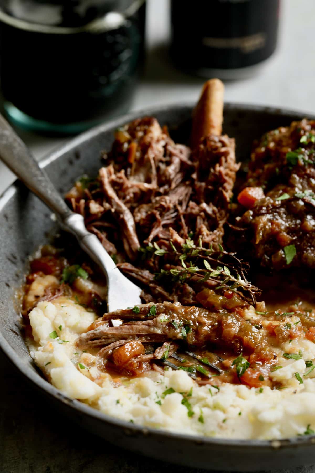 Close-up photo of Stout Braised Beef Short Ribs and Colcannon with fork shredding the beef in gray bowl.