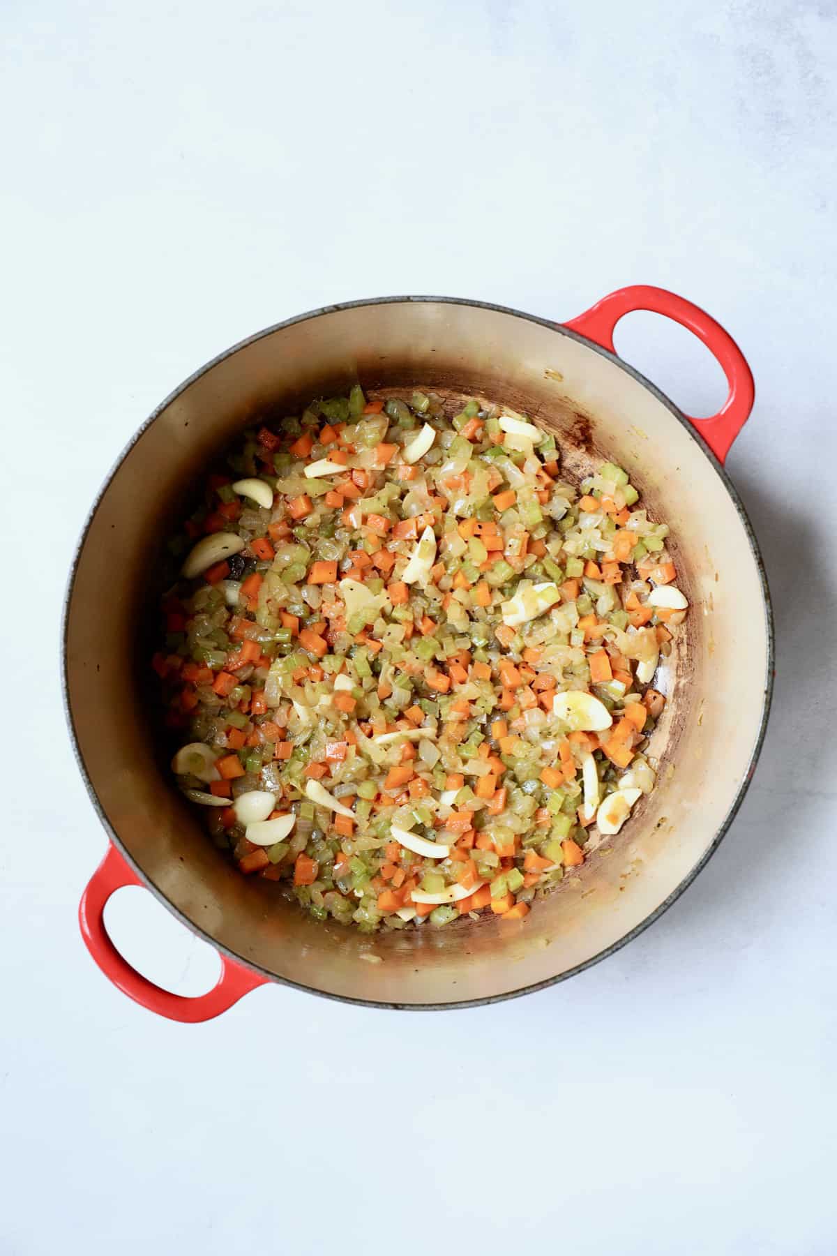 Photo of cooked diced onion, celery, carrot and sliced garlic in red Dutch oven.