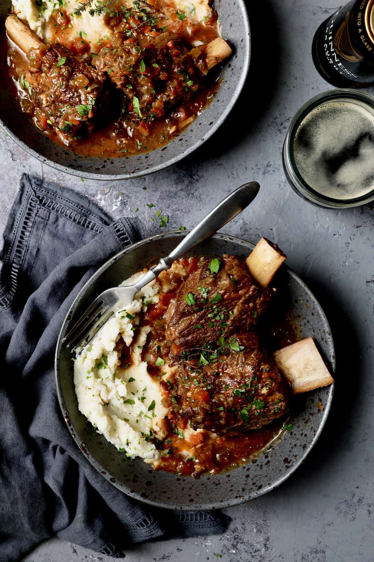 Photo of Stout Braised Beef Short Ribs and Colcannon on gray background with blue napkin and glass of beer.