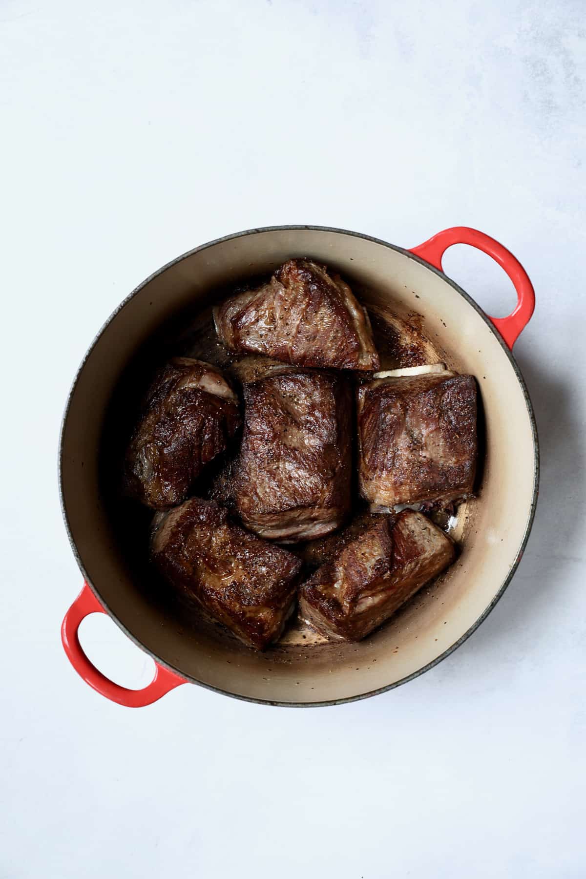 Photo of browned short ribs in red Dutch oven.