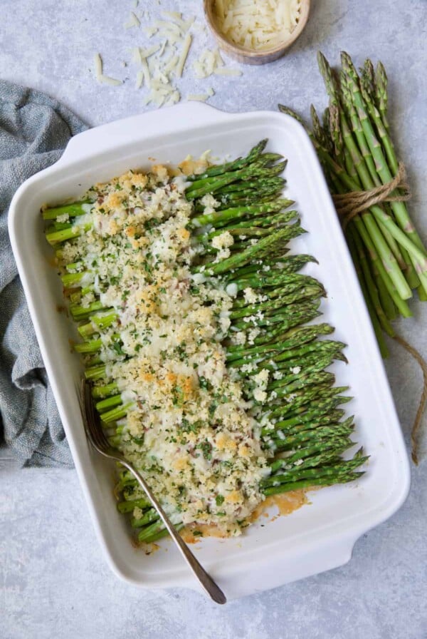 Photo of Asparagus Cordon Bleu in white rectangular baking dish on blue background.