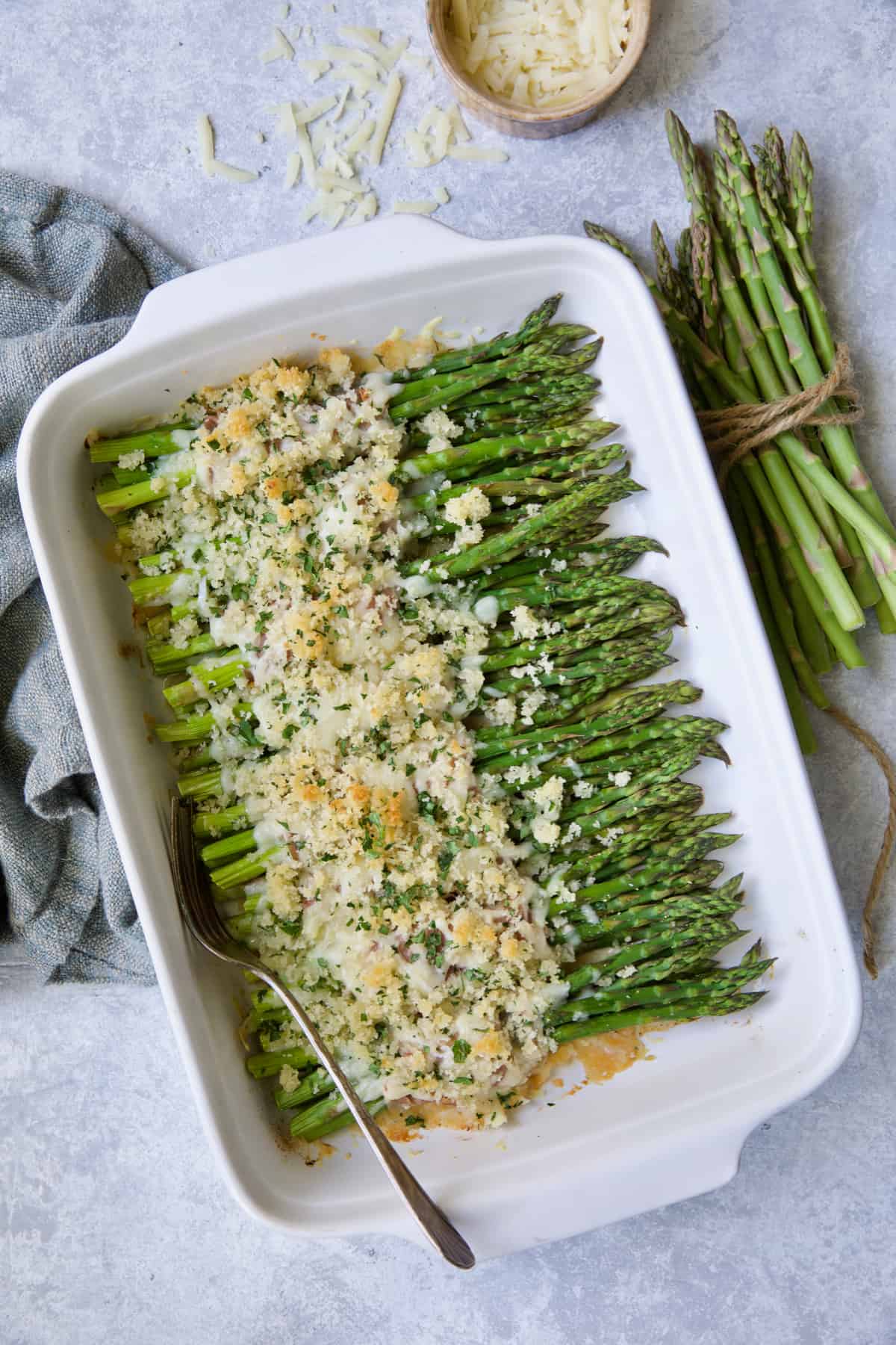Photo of Asparagus Cordon Bleu in white rectangular baking dish on blue background.