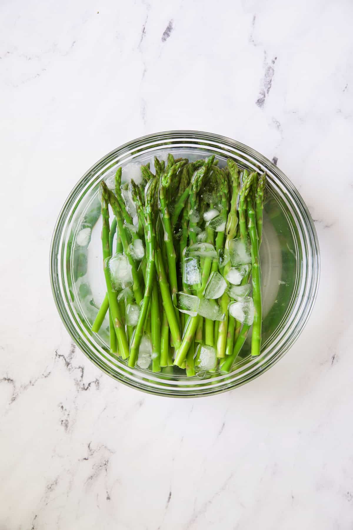 Photo of asparagus in ice bath in glass bowl.