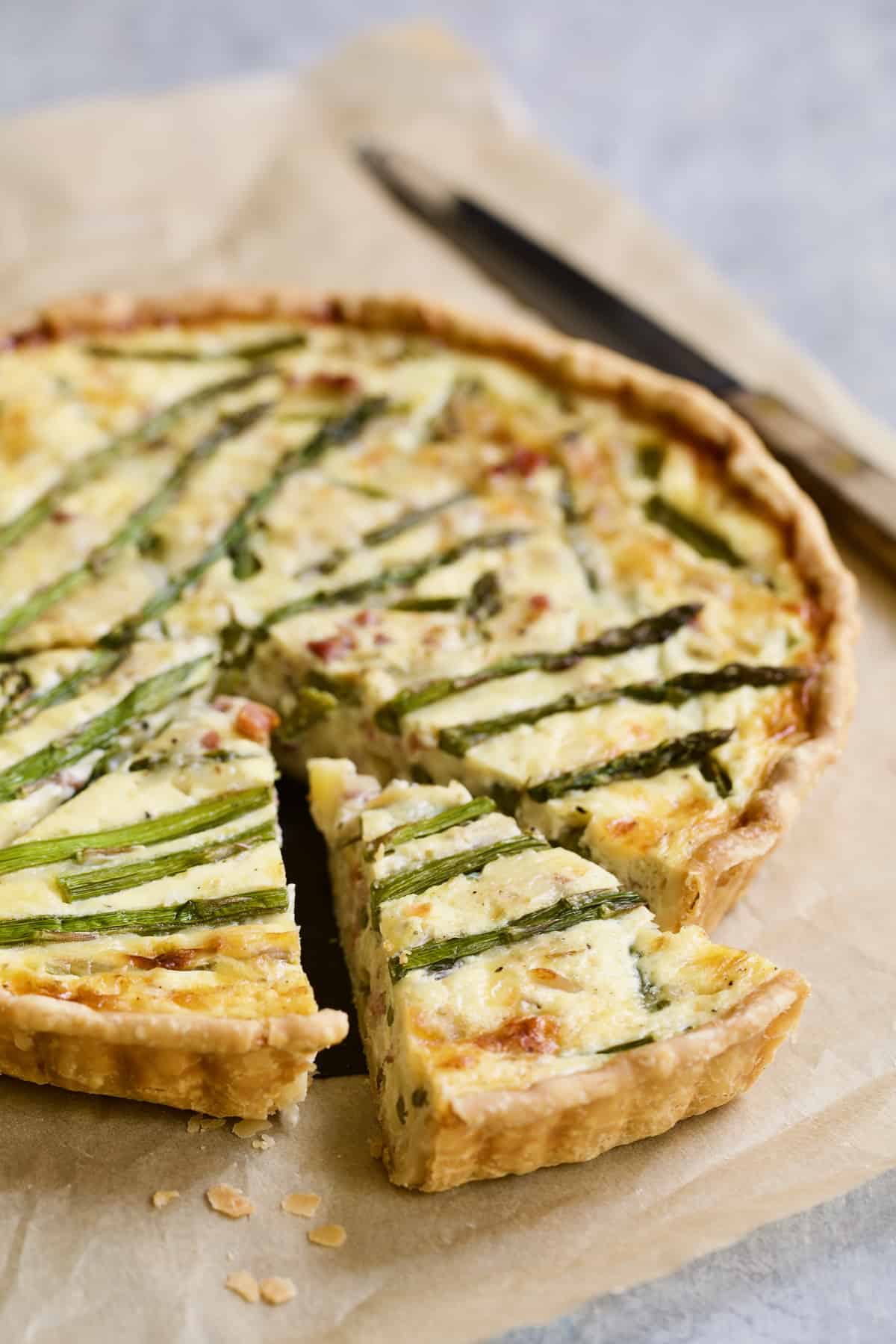 Photo of Asparagus Prosciutto and Fontina Tart on brown parchment paper with three pieces cut.