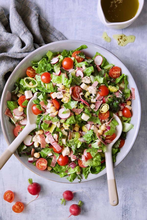 Photo of Italian Chopped Salad with Chicken with tomatoes and radishes scattered around bowl.