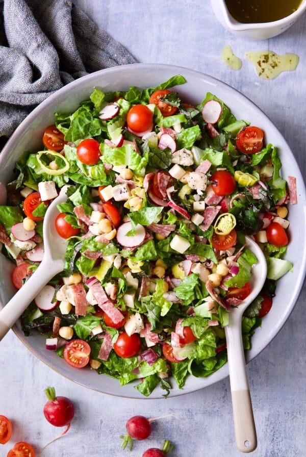 Photo of Italian Chopped Salad with Chicken in gray bowl with serving utensils.