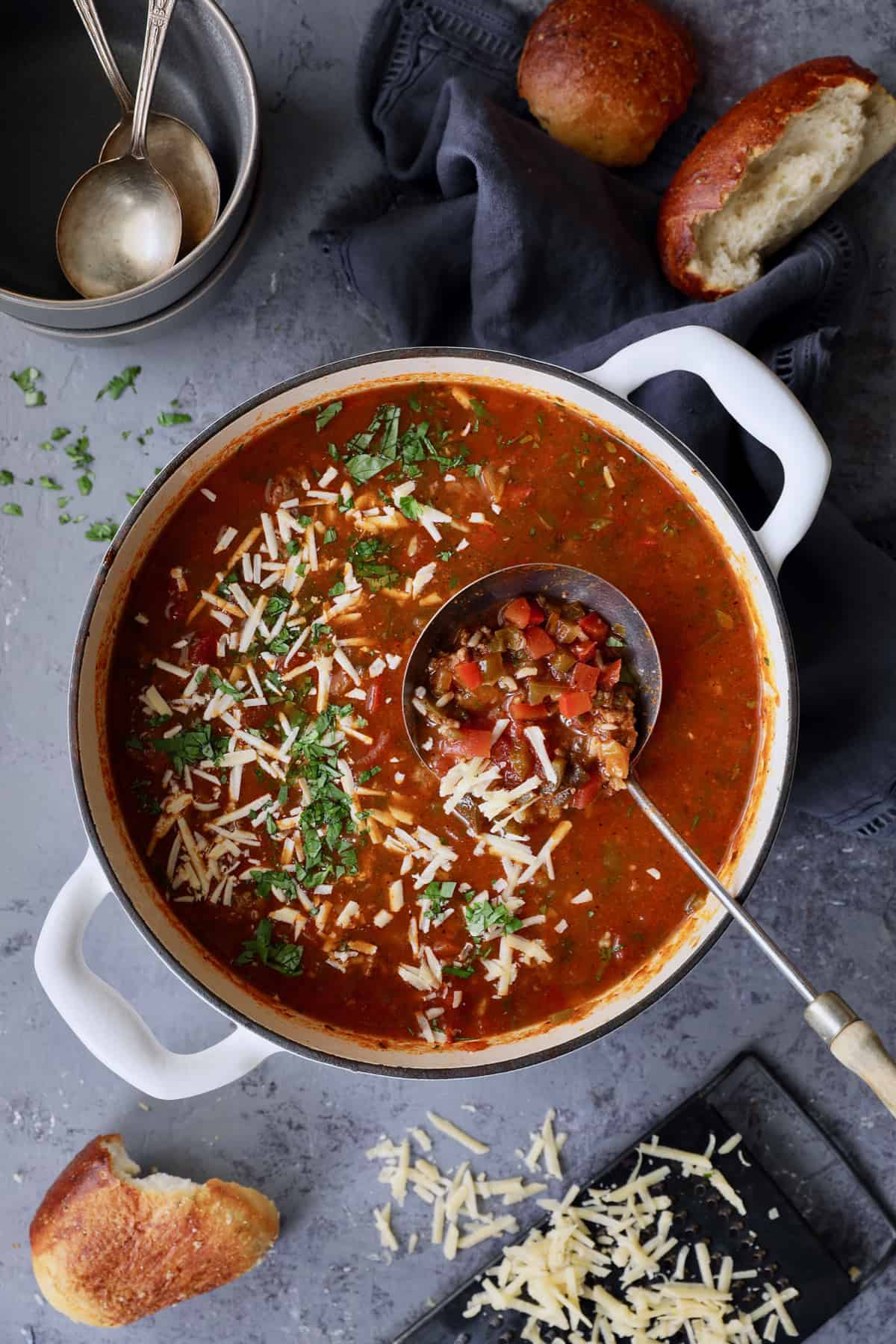 Photo of Southwestern Stuffed Pepper Soup in white Dutch oven on blue background sprinkled with cheese and cilantro.