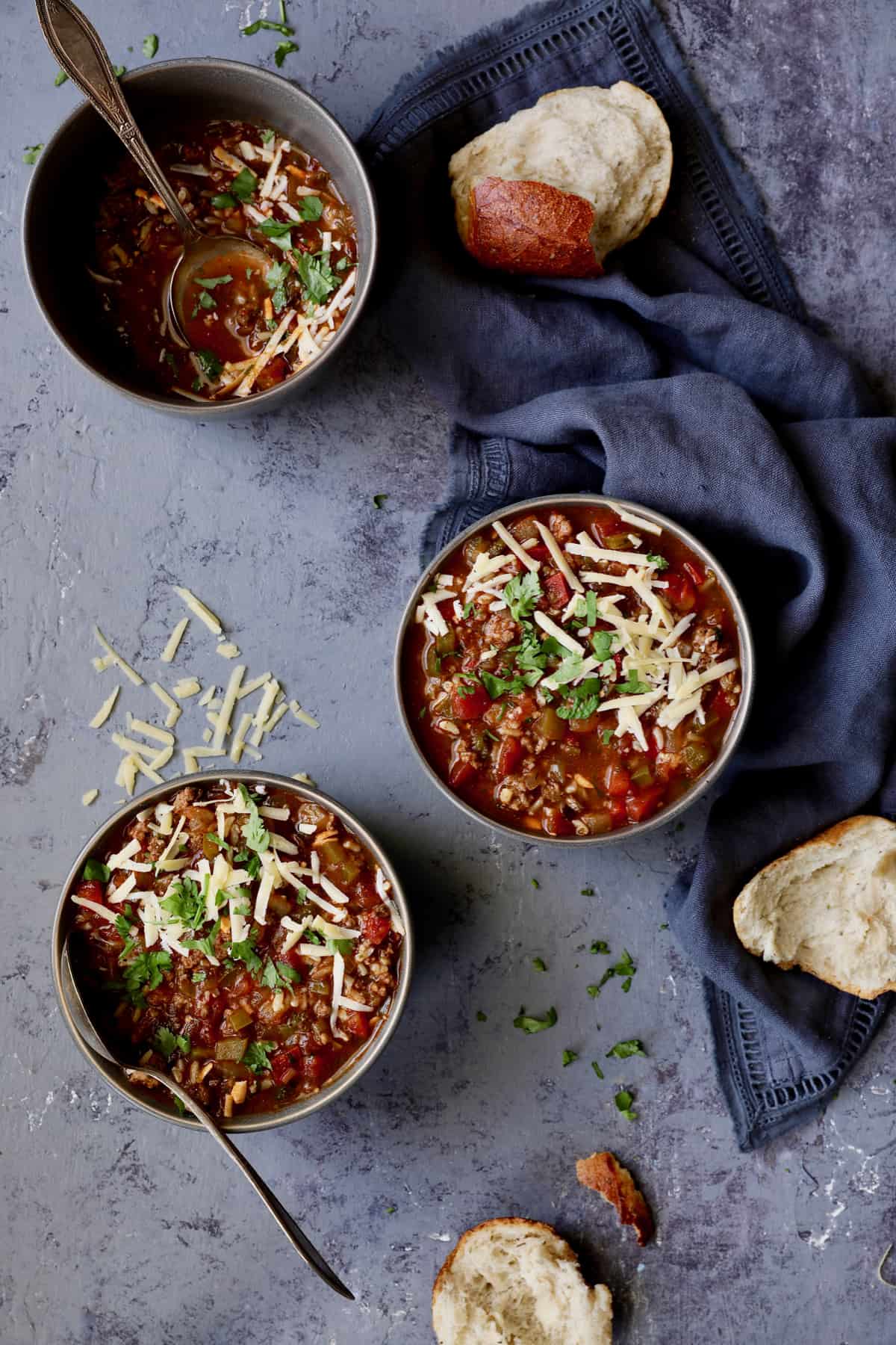 Photo of three bowls of Southwestern Stuffed Pepper Soup in gray bowls topped with cheese and cilantro.