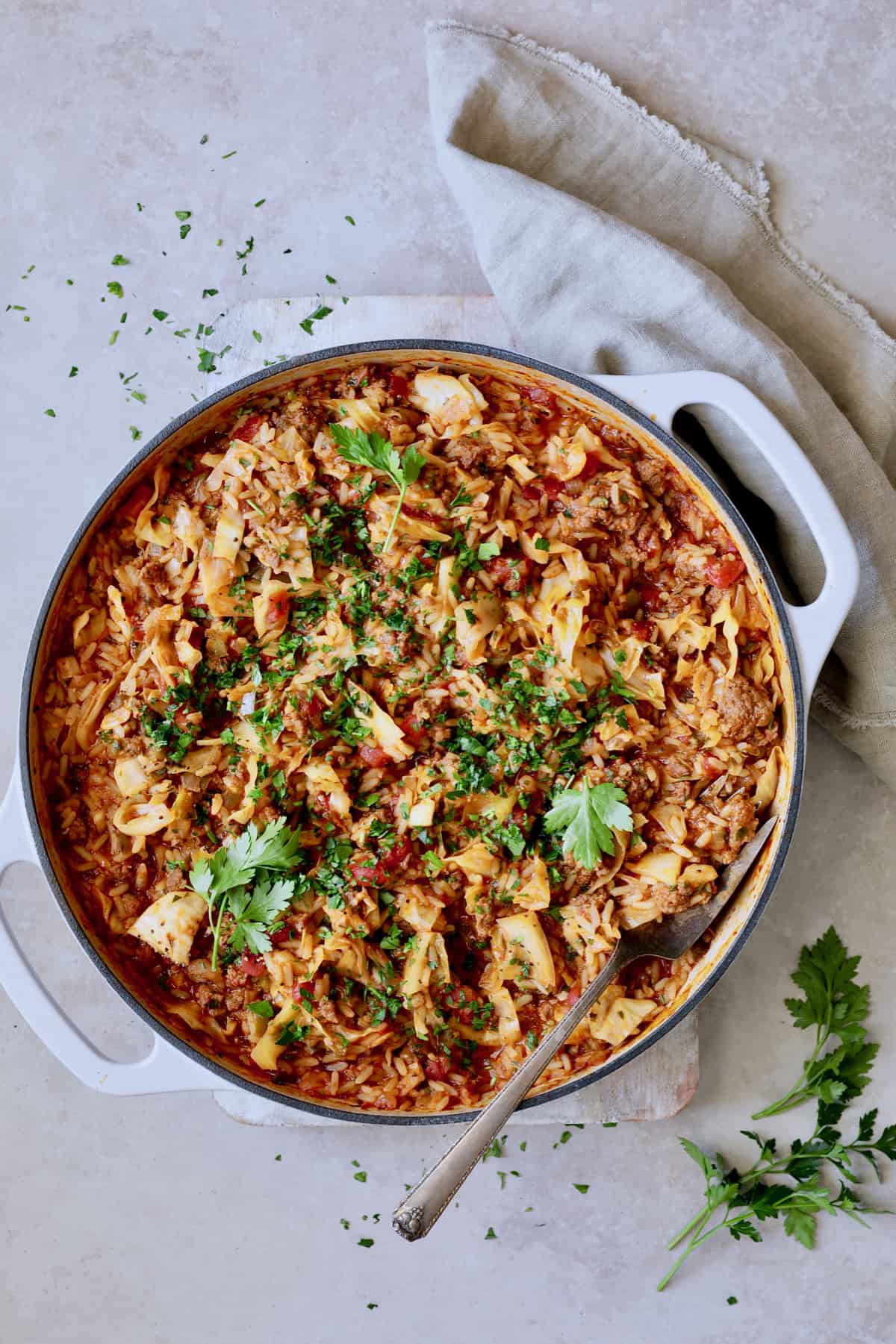 Photo of Unstuffed Chorizo Cabbage Roll Skillet on beige surface garnished with parsley.