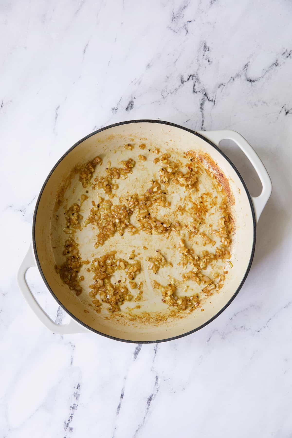 Browned cooked shallots in white enamel cast iron skillet.