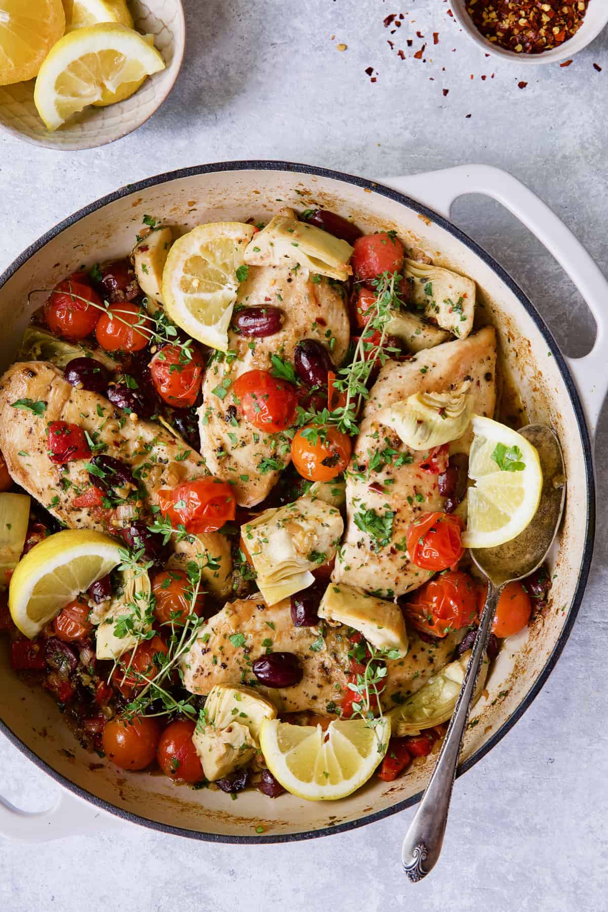 Easy Skillet Mediterranean Chicken in white enamel cast iron skillet garnished with fresh thyme and lemon wedges.