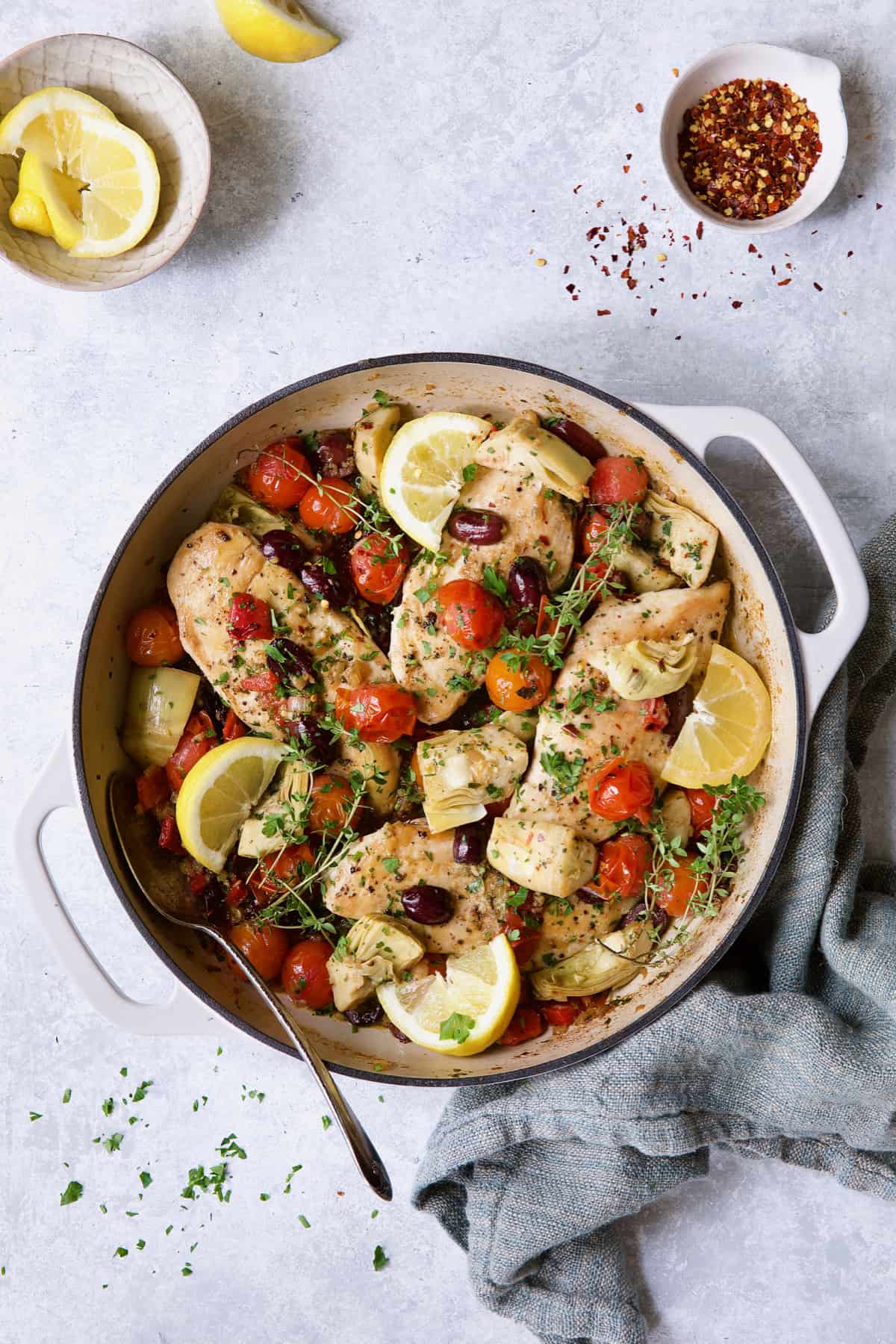 Easy Skillet Mediterranean Chicken on light blue background with blue towel garnished with lemon wedges and thyme.