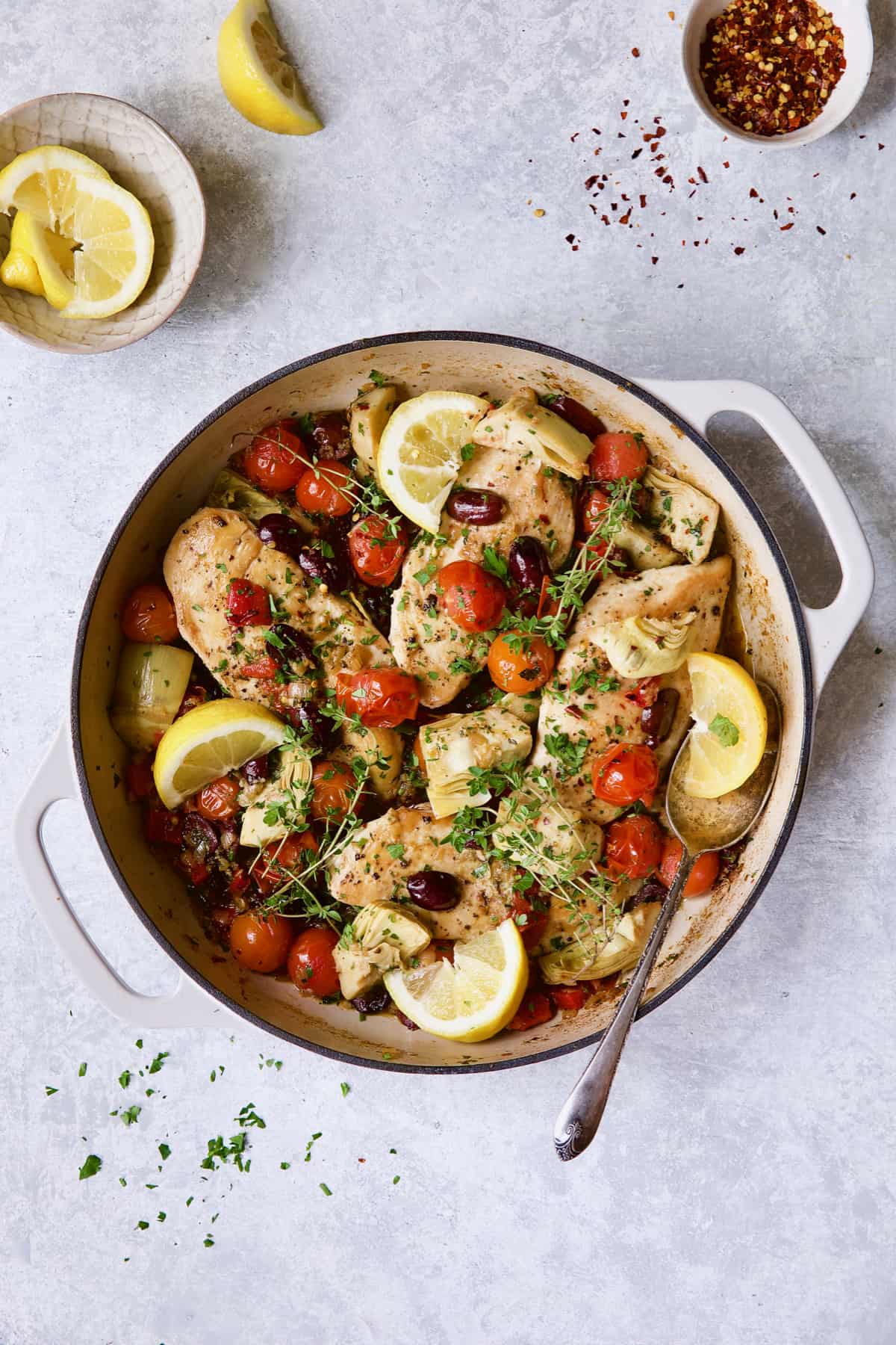 Easy Skillet Mediterranean Chicken in white enamel skillet garnished with lemon wedges and fresh thyme.