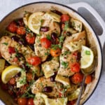 Photo of Easy Skillet Mediterranean Chicken in white enamel cast iron skillet garnished with fresh thyme and lemon wedges.