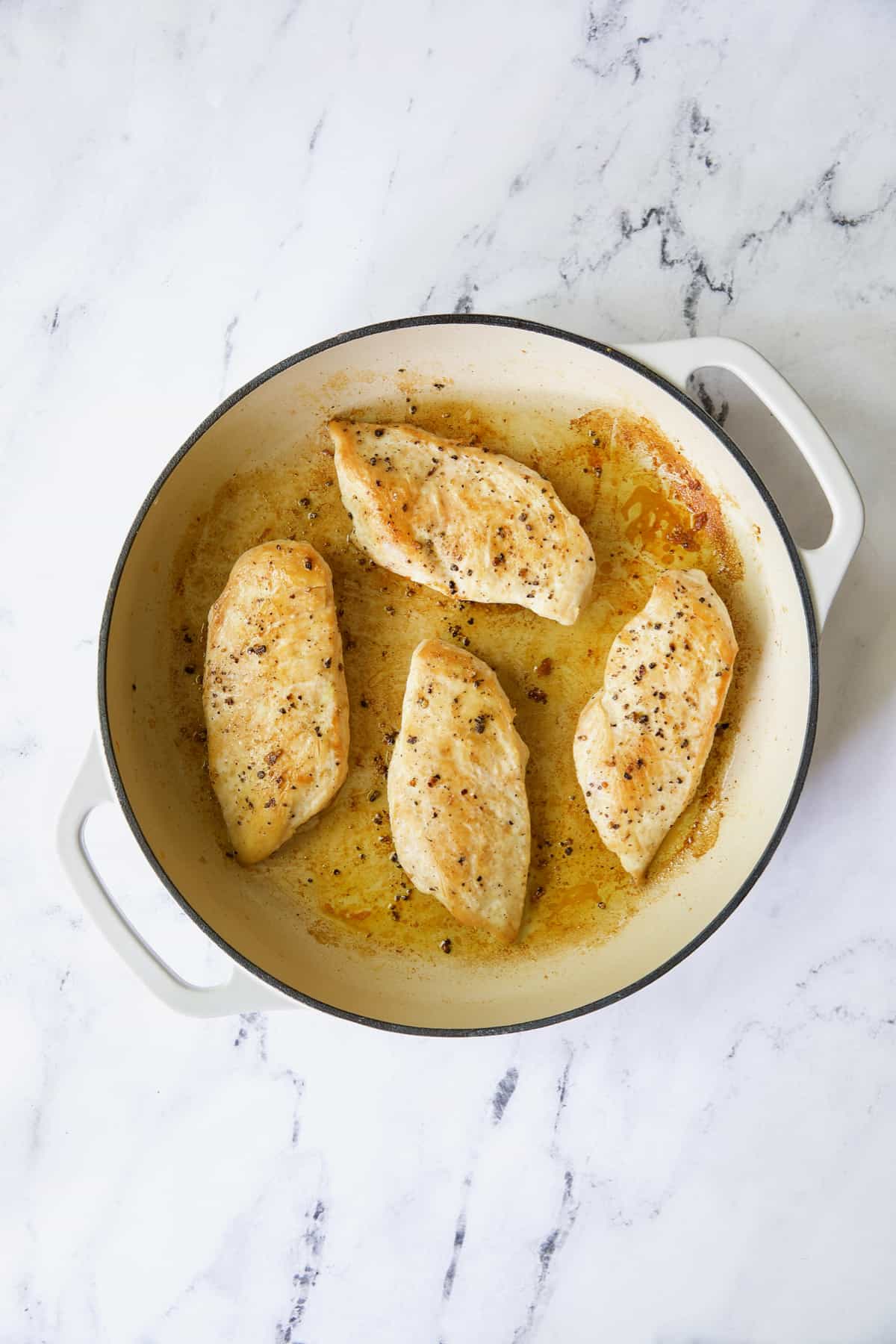 Four boneless skinless chicken breasts in white enamel skillet.