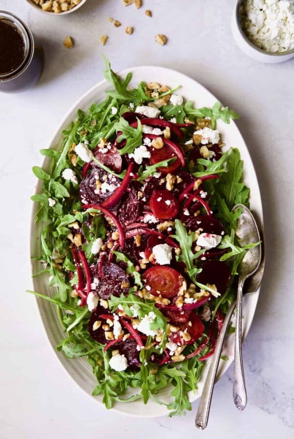 Photo of Roasted Beet Salad with Walnuts Goat Cheese and Honey Balsamic Dressing on white oval platter with serving utensils.