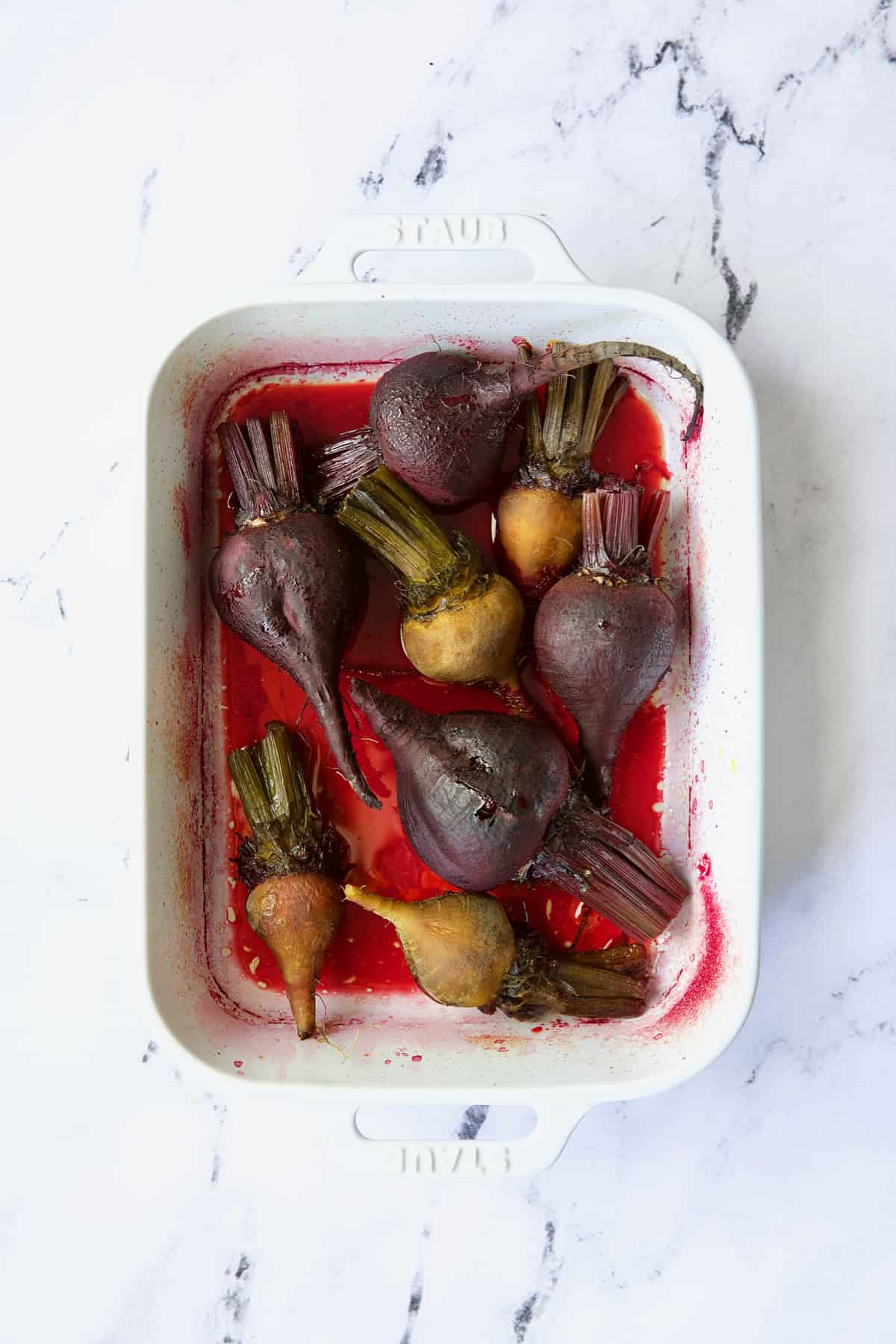 Roasted red and yellow beets in white baking dish.