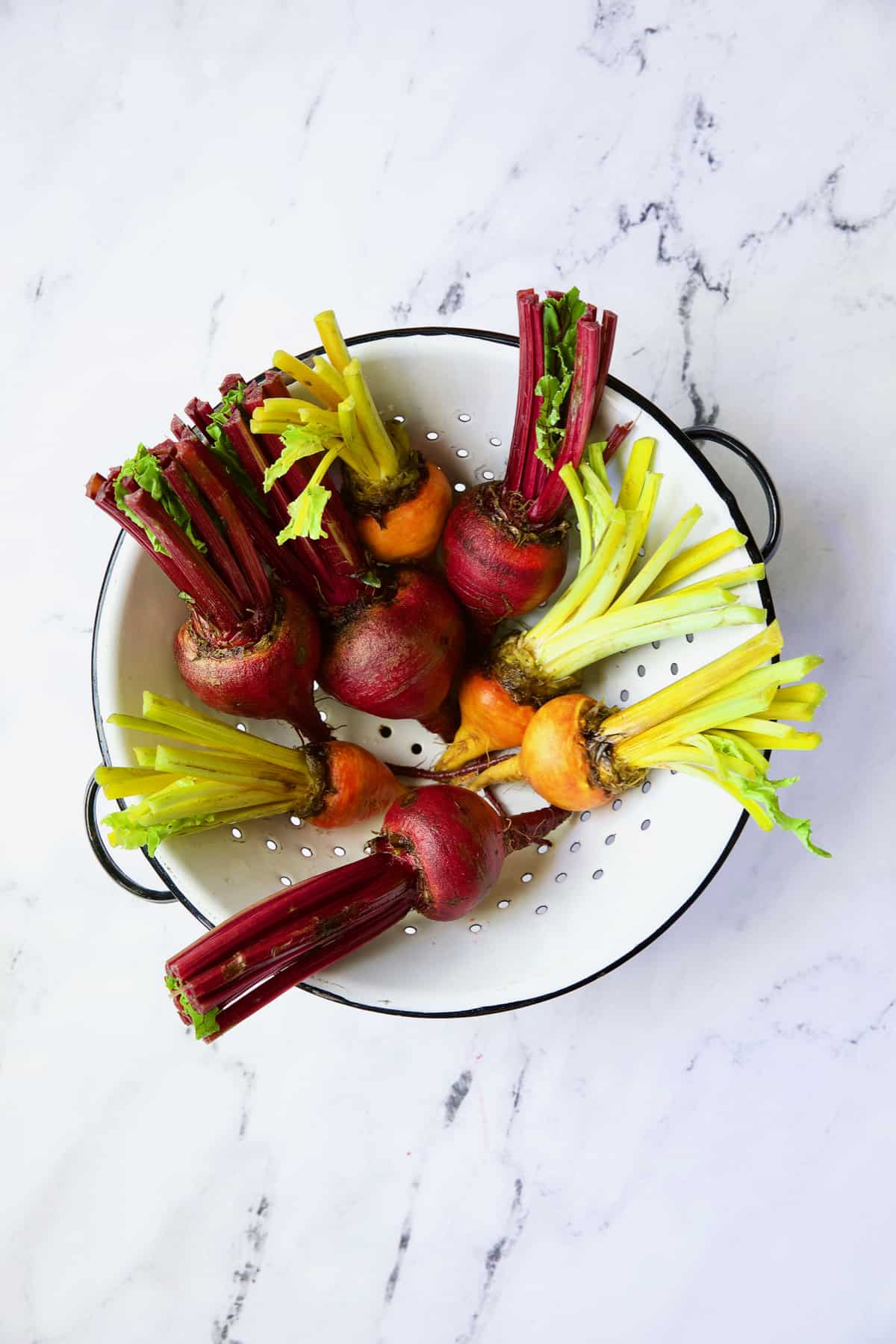 Uncooked red and yellow beets in white colander.