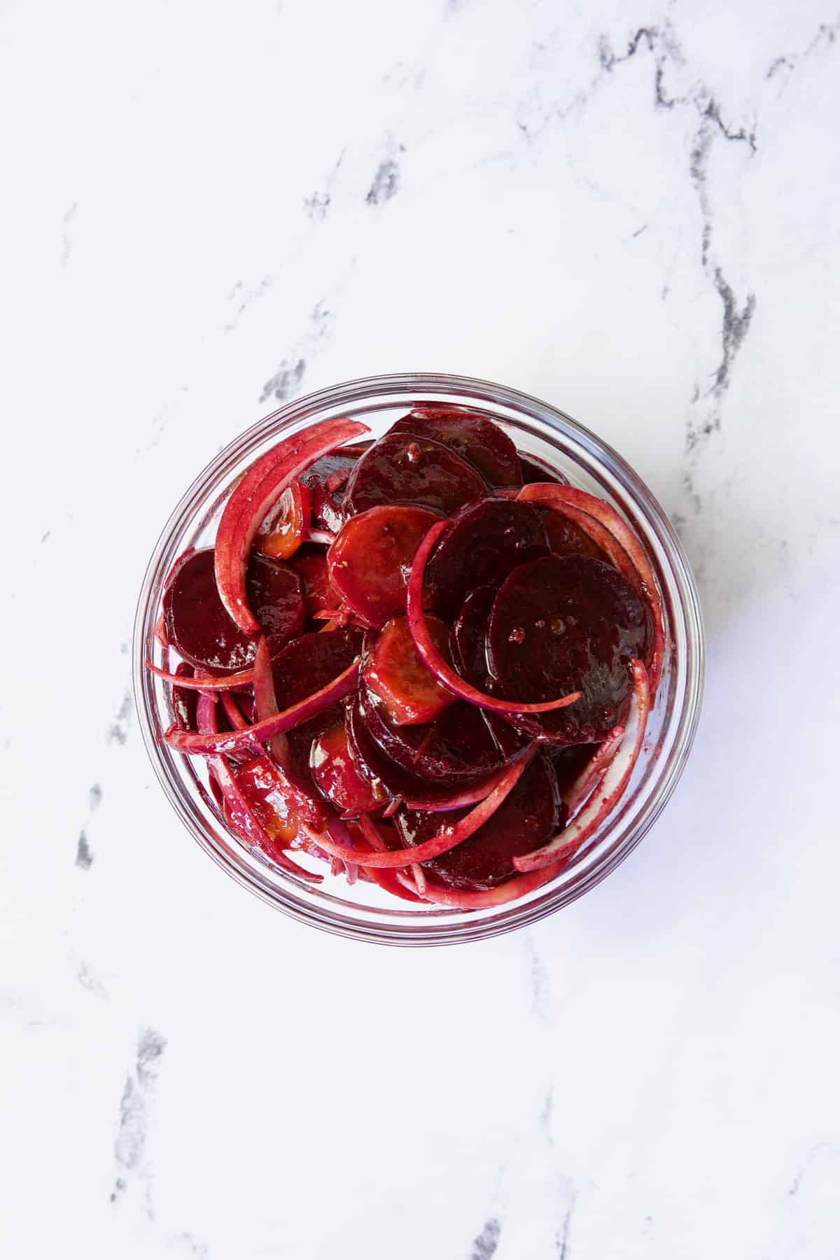 Beets and onions tossed with dressing in glass bowl.