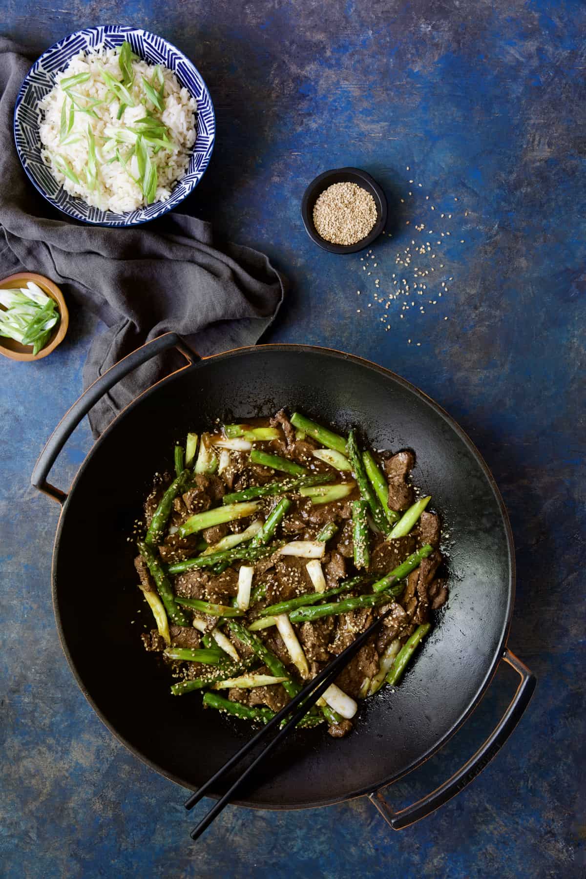 Sesame Beef and Asparagus Stir-Fry with bowl of rice and small bowls of scallions and sesame seeds.