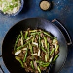 Photo of Sesame Beef and Asparagus Stir-Fry in cast iron wok on bright blue background.