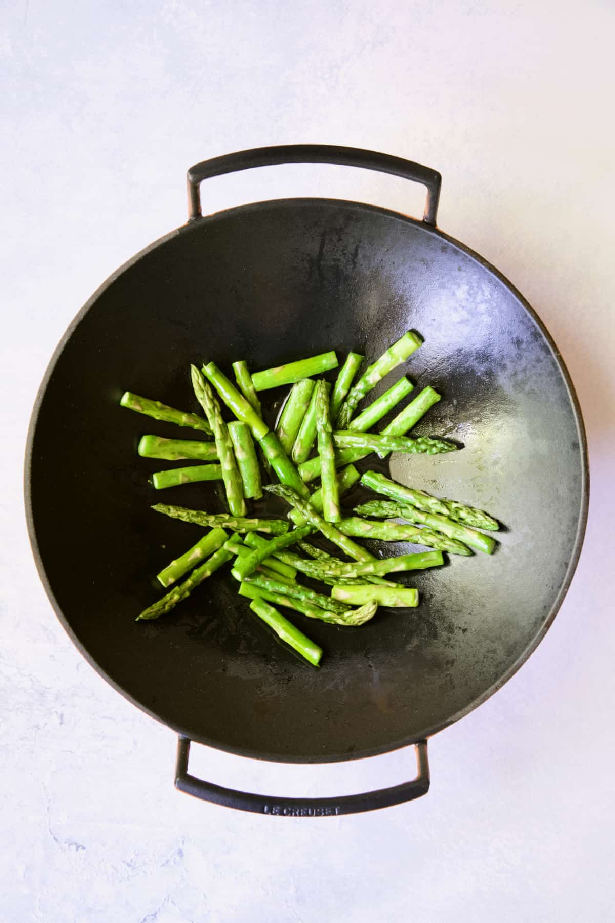 Asparagus being cooked in cast iron wok.