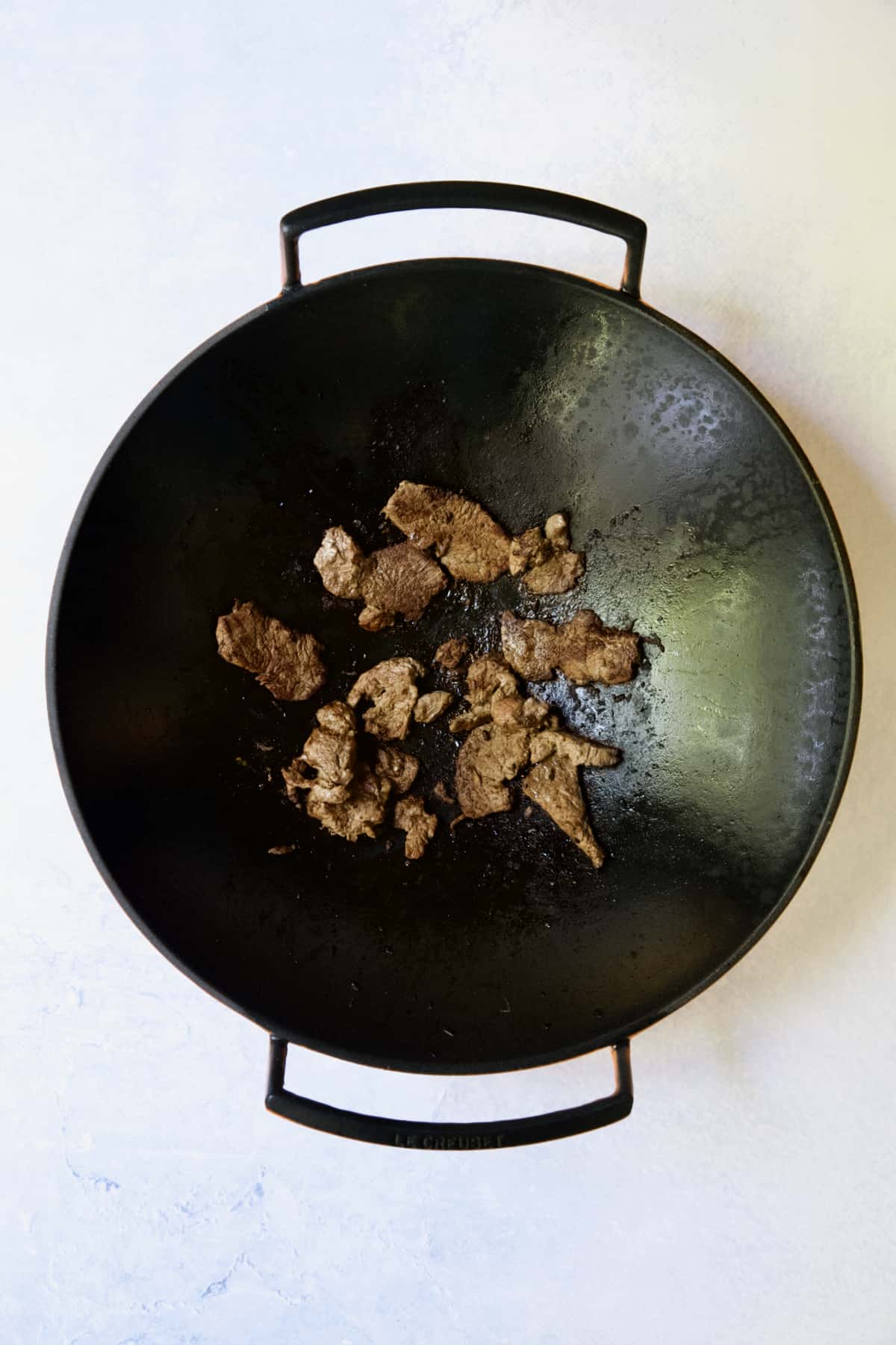 Beef being browned in cast iron wok.