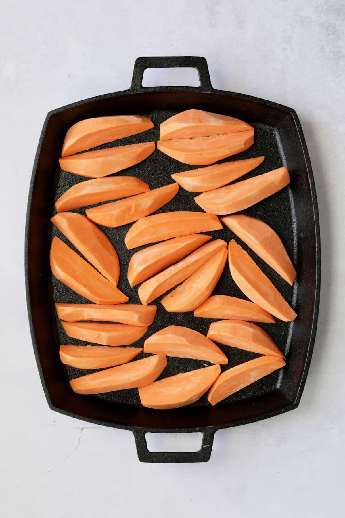 Sweet potato wedges on cast iron pan before being roasted.
