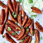 Photo of Southwestern Sweet Potato Wedges on white parchment paper with Cilantro - Avocado Sour Cream.