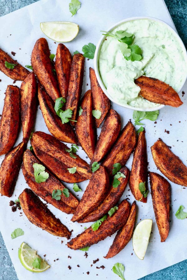 Photo of Southwestern Sweet Potato Wedges on white parchment paper with Cilantro - Avocado Sour Cream.