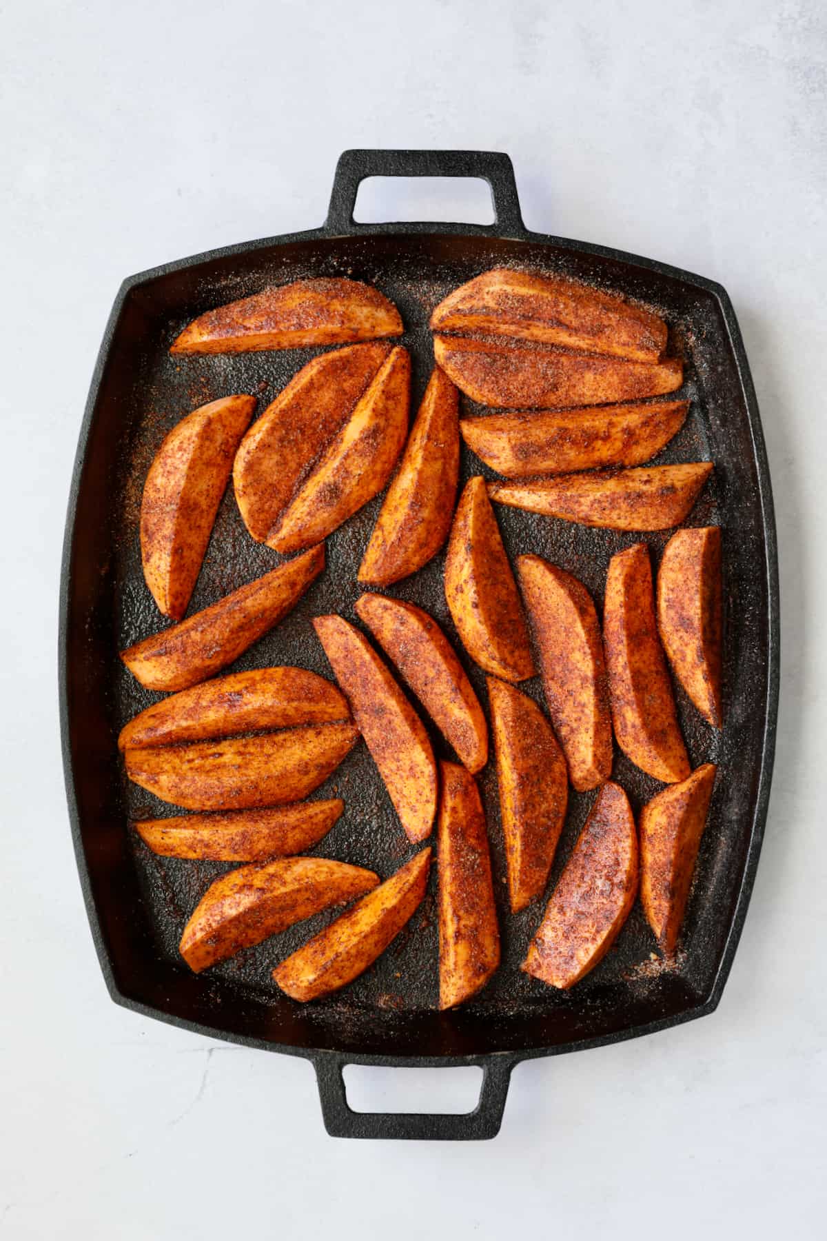 Southwestern Sweet Potato Wedges on cast iron pan with seasoning mix before being roasted.