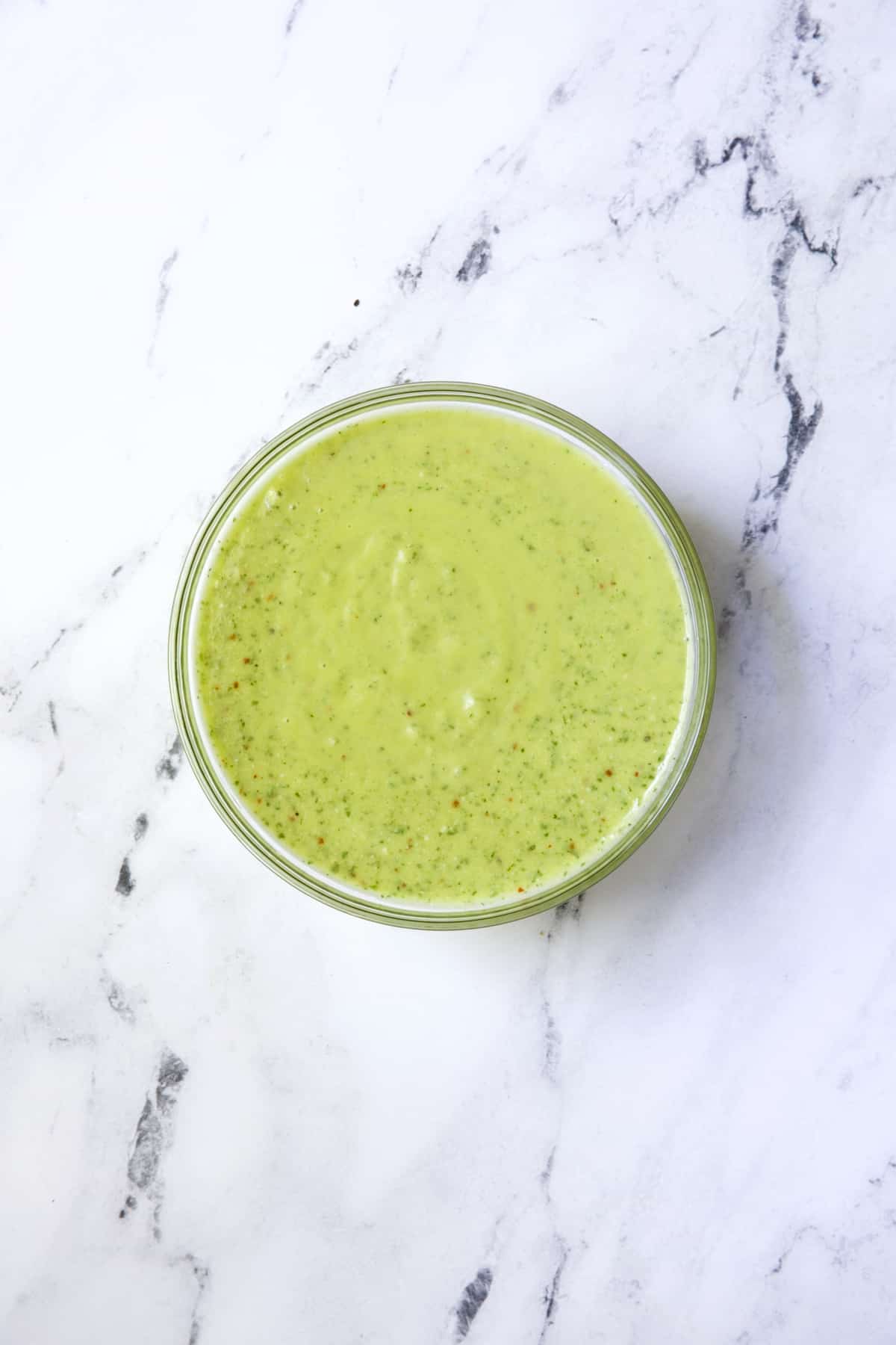 Parmesan Herb Vinaigrette in glass jar on white marble background.
