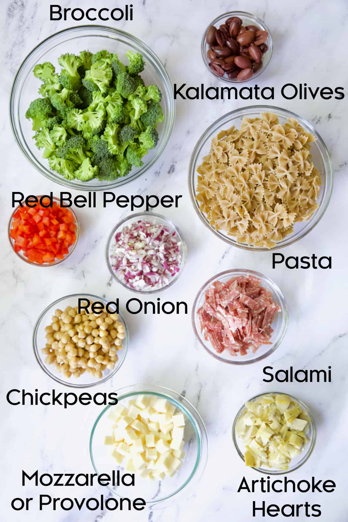 Photo of ingredients for Antipasto Pasta Broccoli Salad in glass bowls.