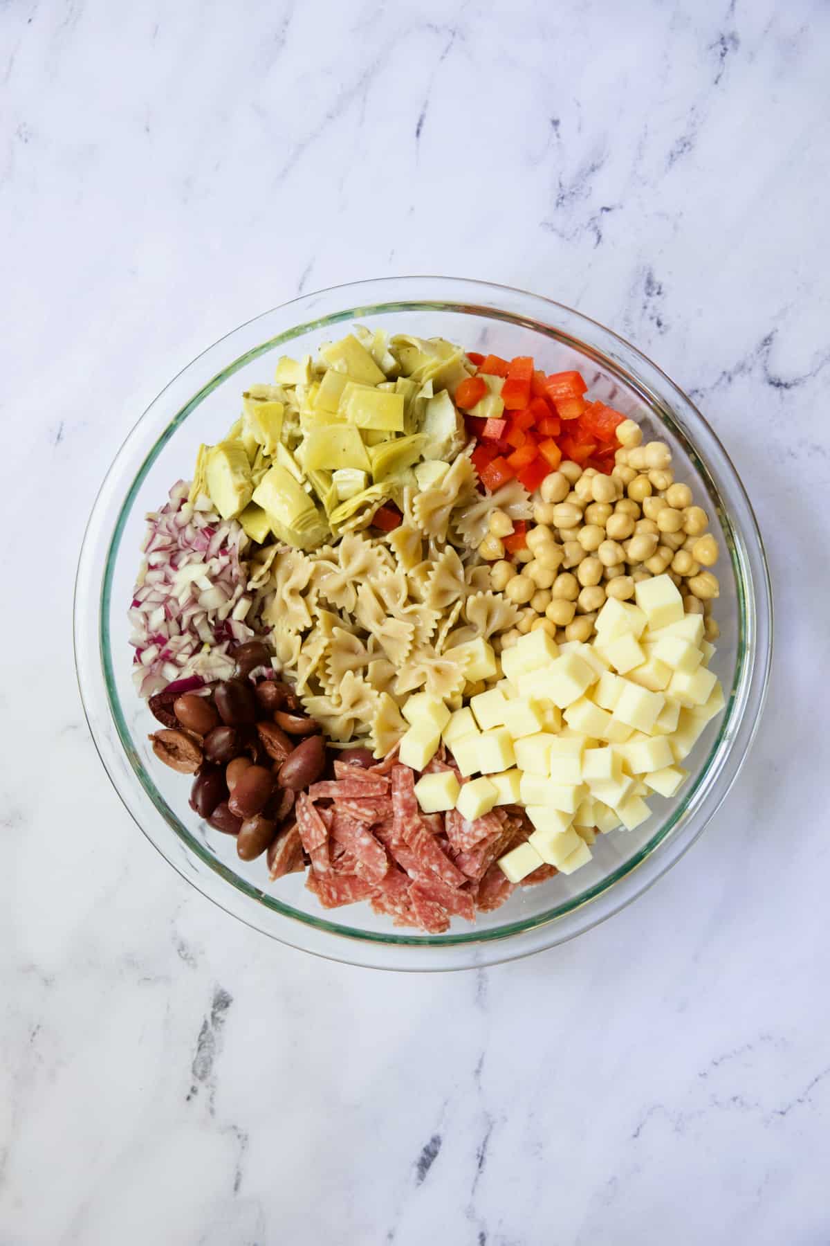 Ingredients for Antipasto Pasta Salad with Parmesan Herb Vinaigrette in glass bowl before being combined.