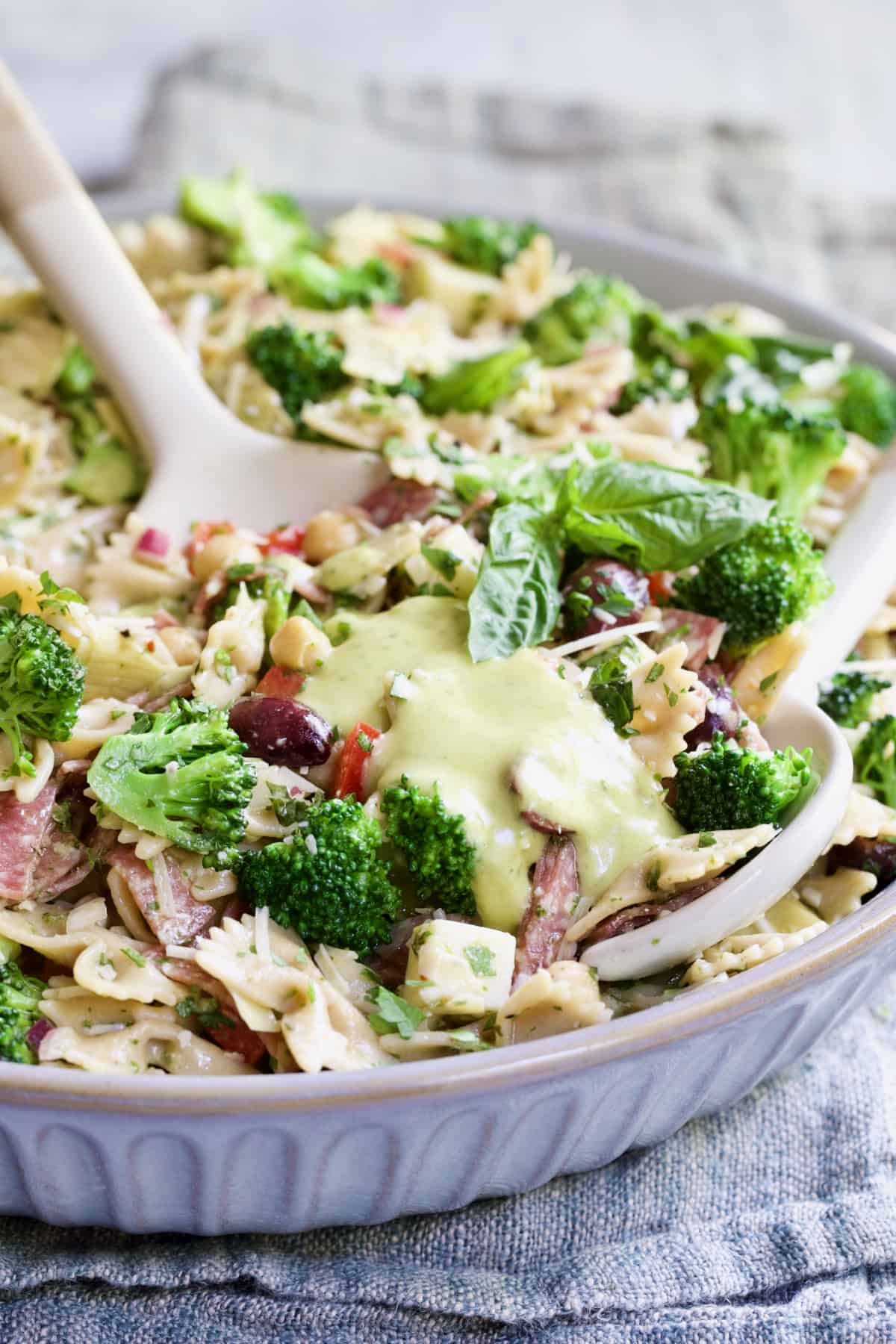 Antipasto Pasta Broccoli Salad with Parmesan Herb Vinaigrette poured over the top about to be mixed with serving utensils.