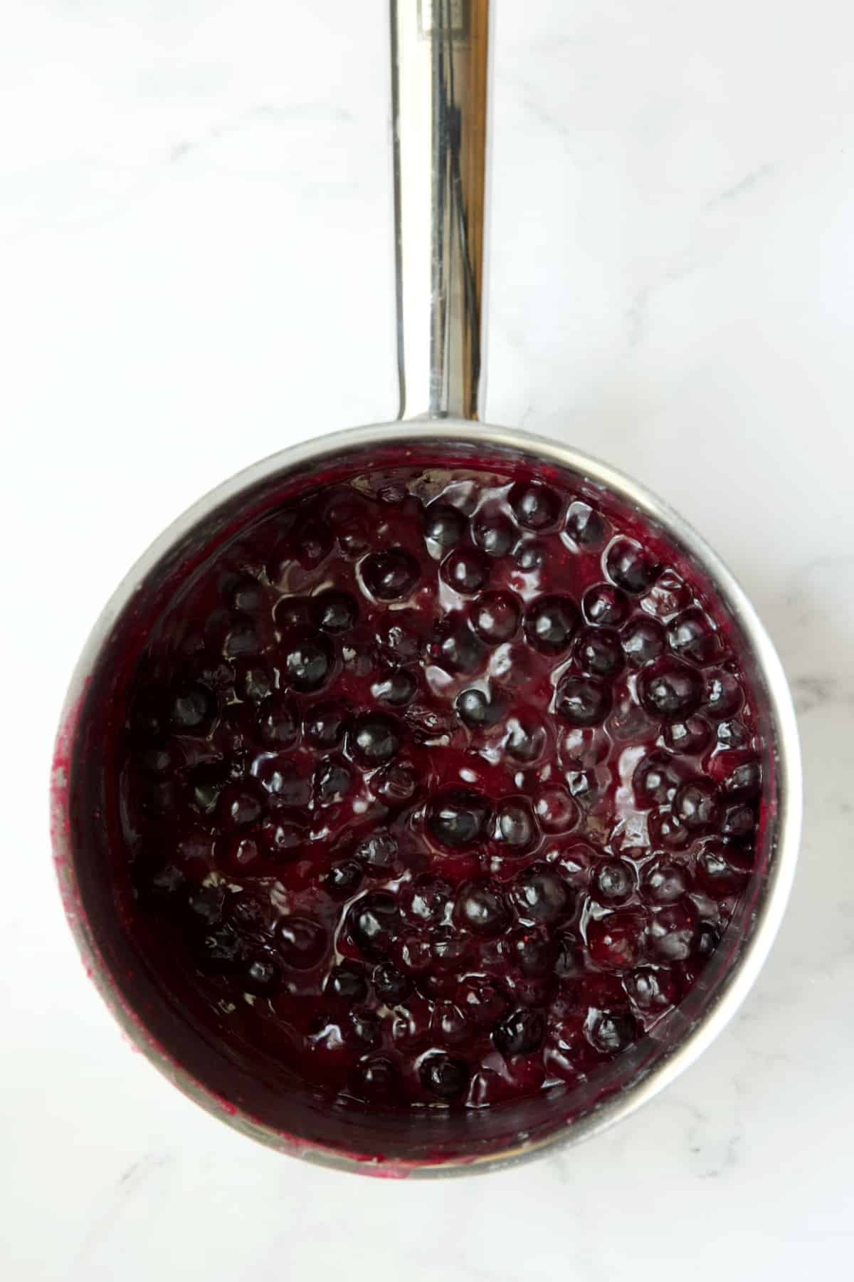 Process photo of blueberries in stainless steel saucepan.