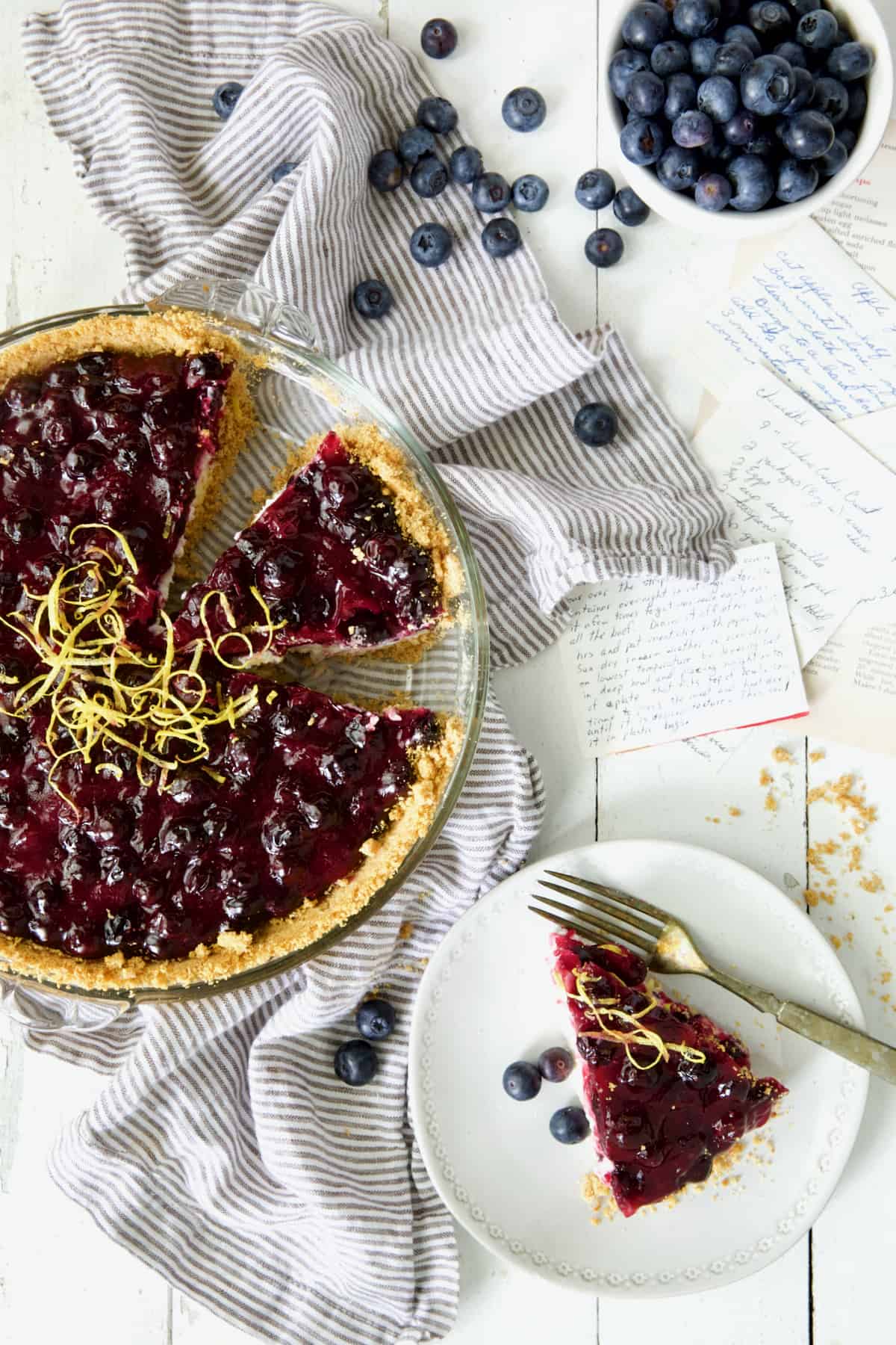 Photo of Blueberry Cream Cheese Pie on white background with pieces cut and one on white plate.