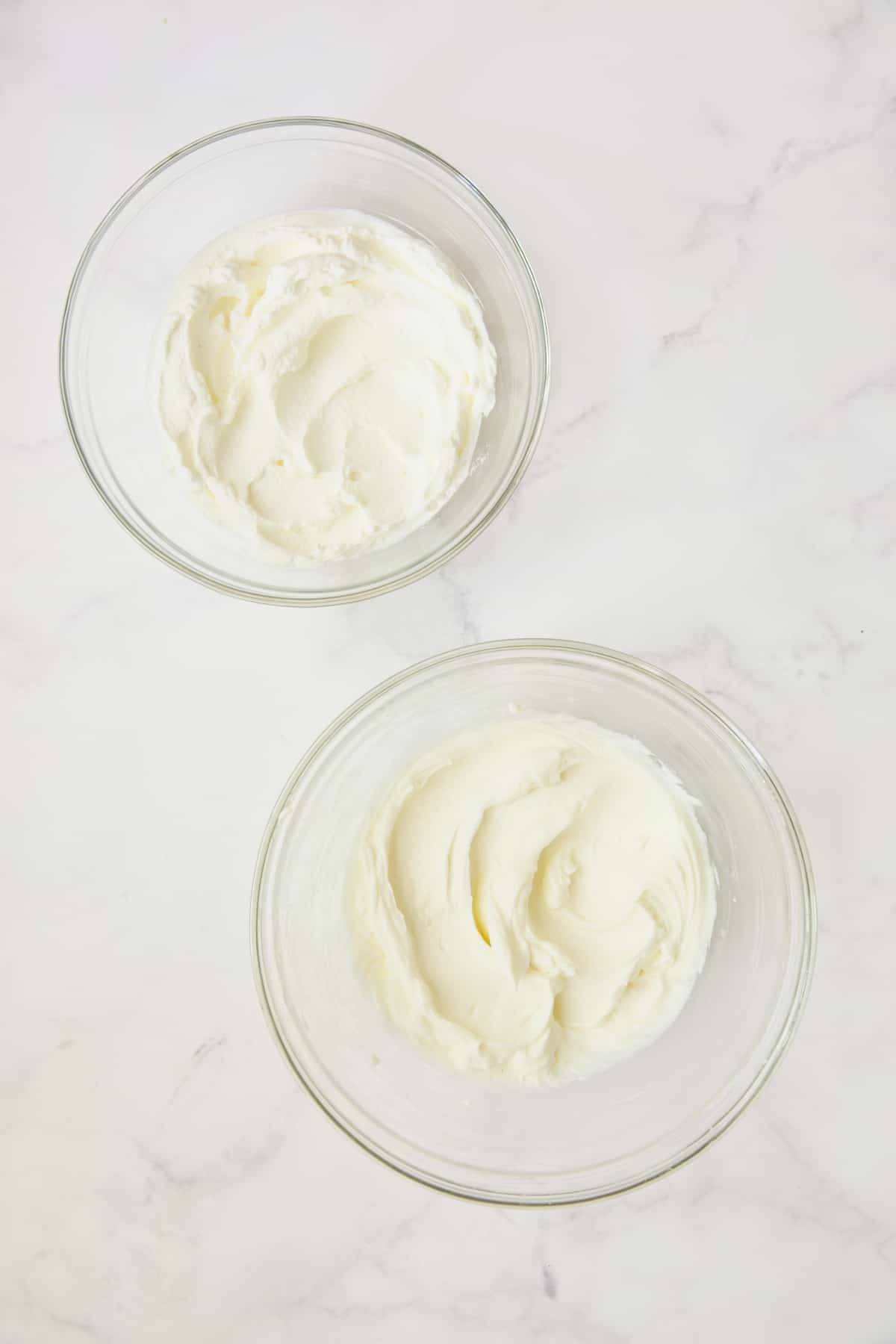 Process photo of whipped cream and cream cheese in glass bowls.