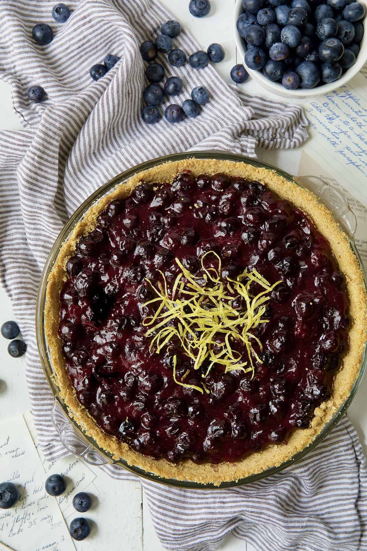 Blueberry Cream Cheese Pie on striped towel with blueberries scattered about.
