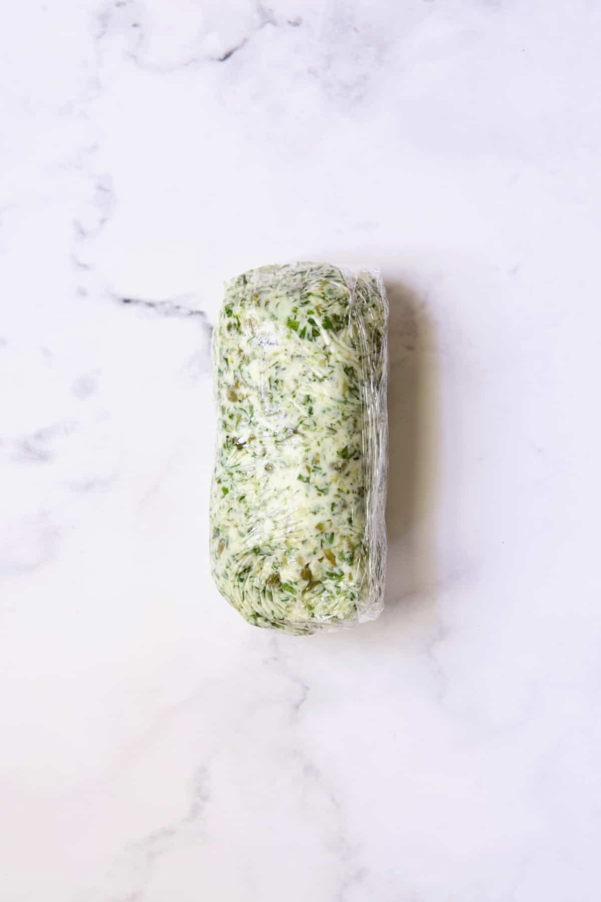 Herb - Caper Butter formed into a log wrapped in plastic wrap.