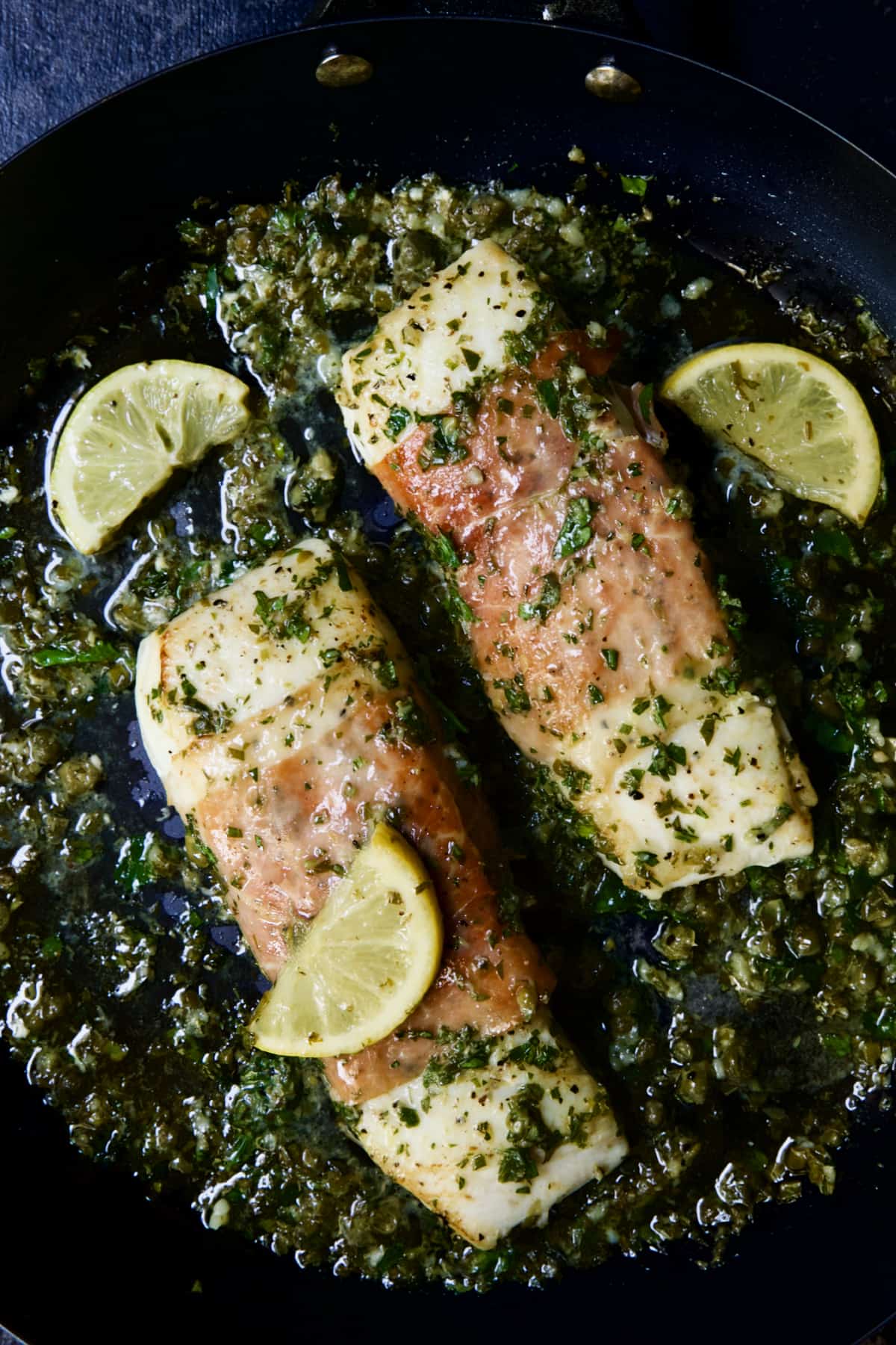 Prosciutto-Wrapped Halibut with Herb - Caper Butter with lemon wedges.