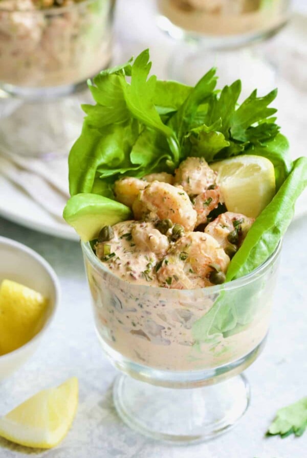 Photo of Sriracha Shrimp Remoulade Cocktail with lettuce, celery leaves, avocado wedge and lemon wedge.