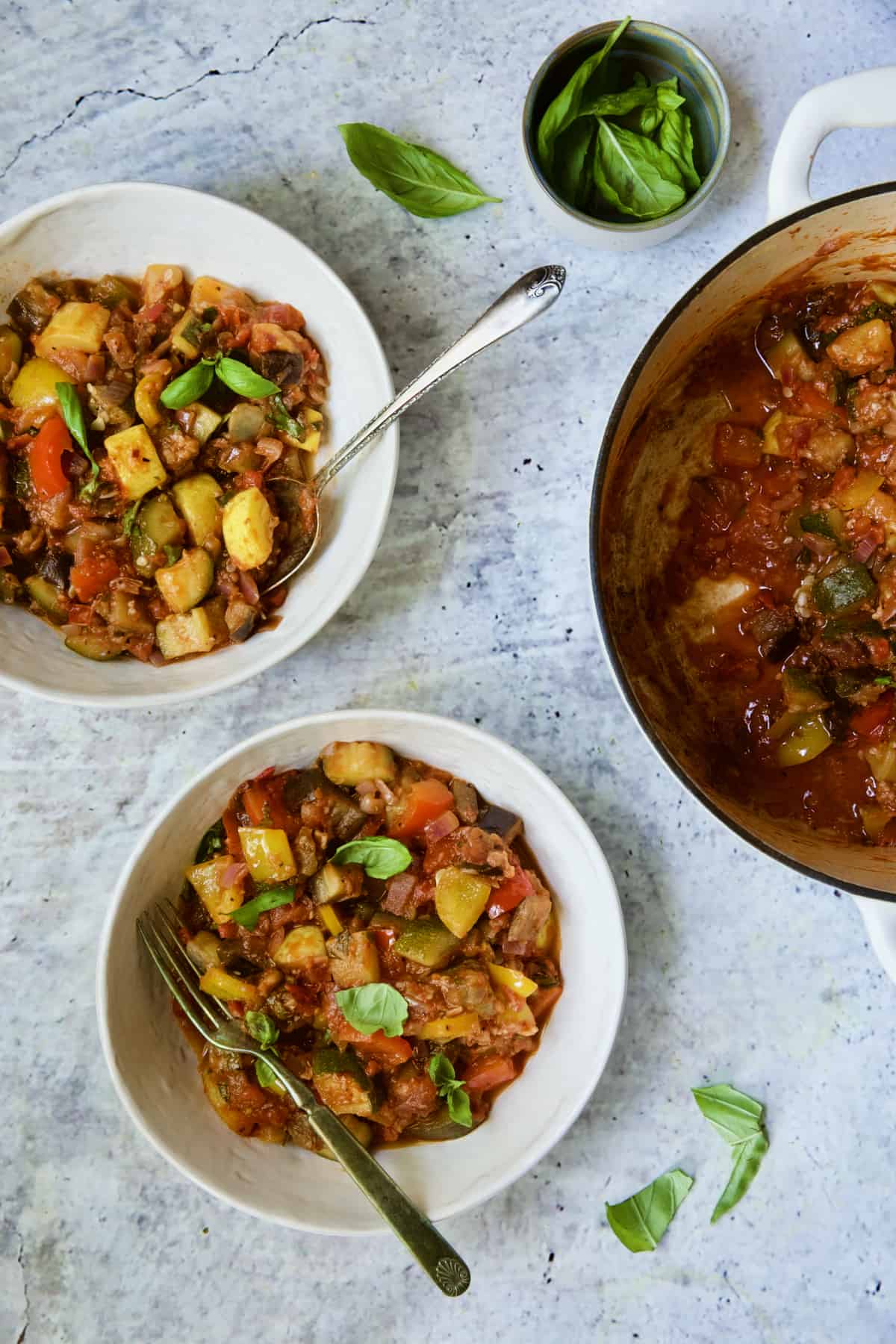 Two servings of Classic French Ratatouille in white bowls garnished with fresh basil.