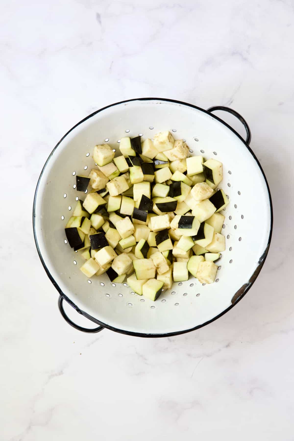 Cubed eggplant in white colander.