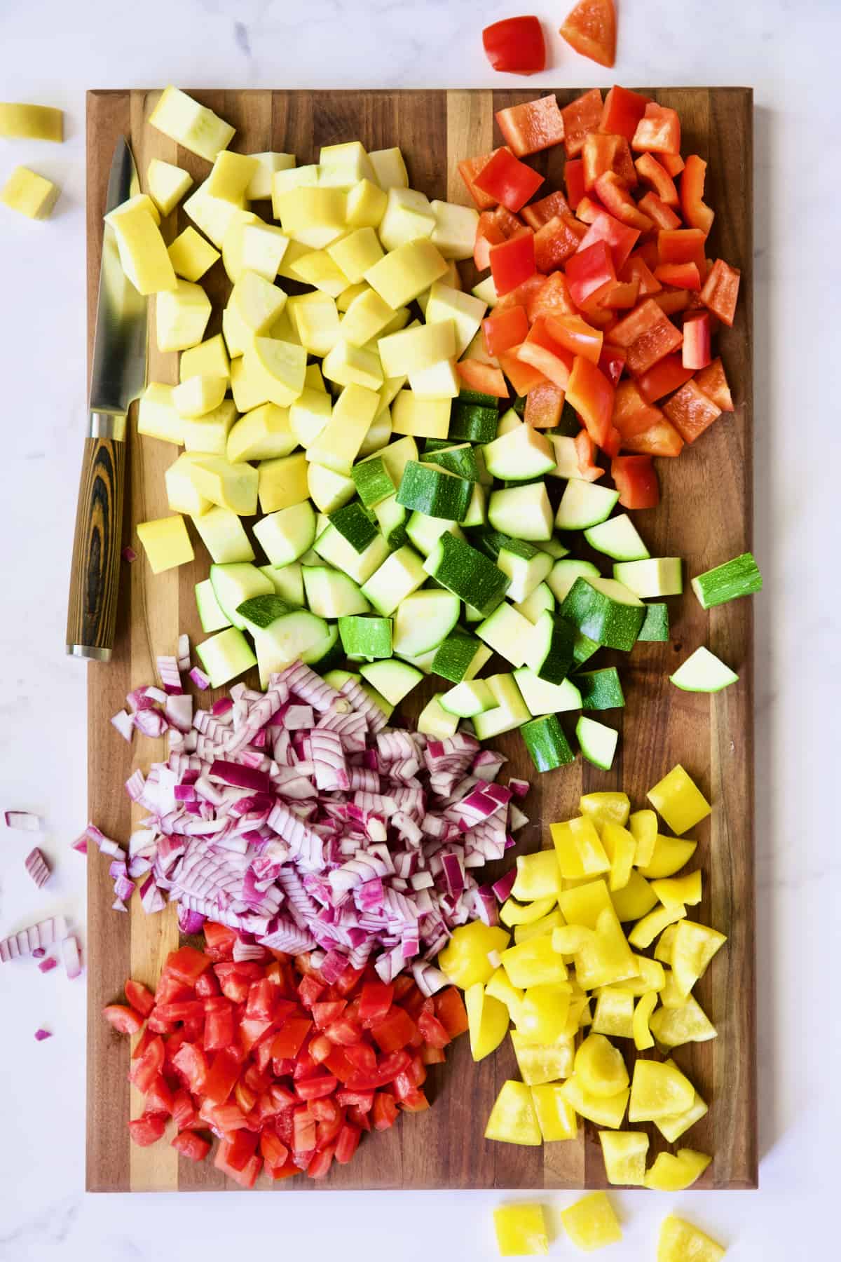 Vegetables cut up for ratatouille on dark wood cutting board.